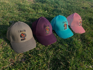 Four different color hats (grey, maroon, blue, and pink) displayed on green grass outdoors.