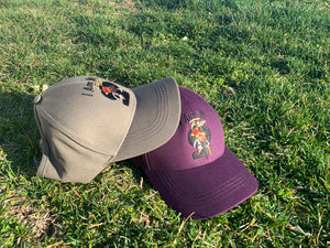 Grey and purple ponytail baseball caps displayed on green grass outdoors.