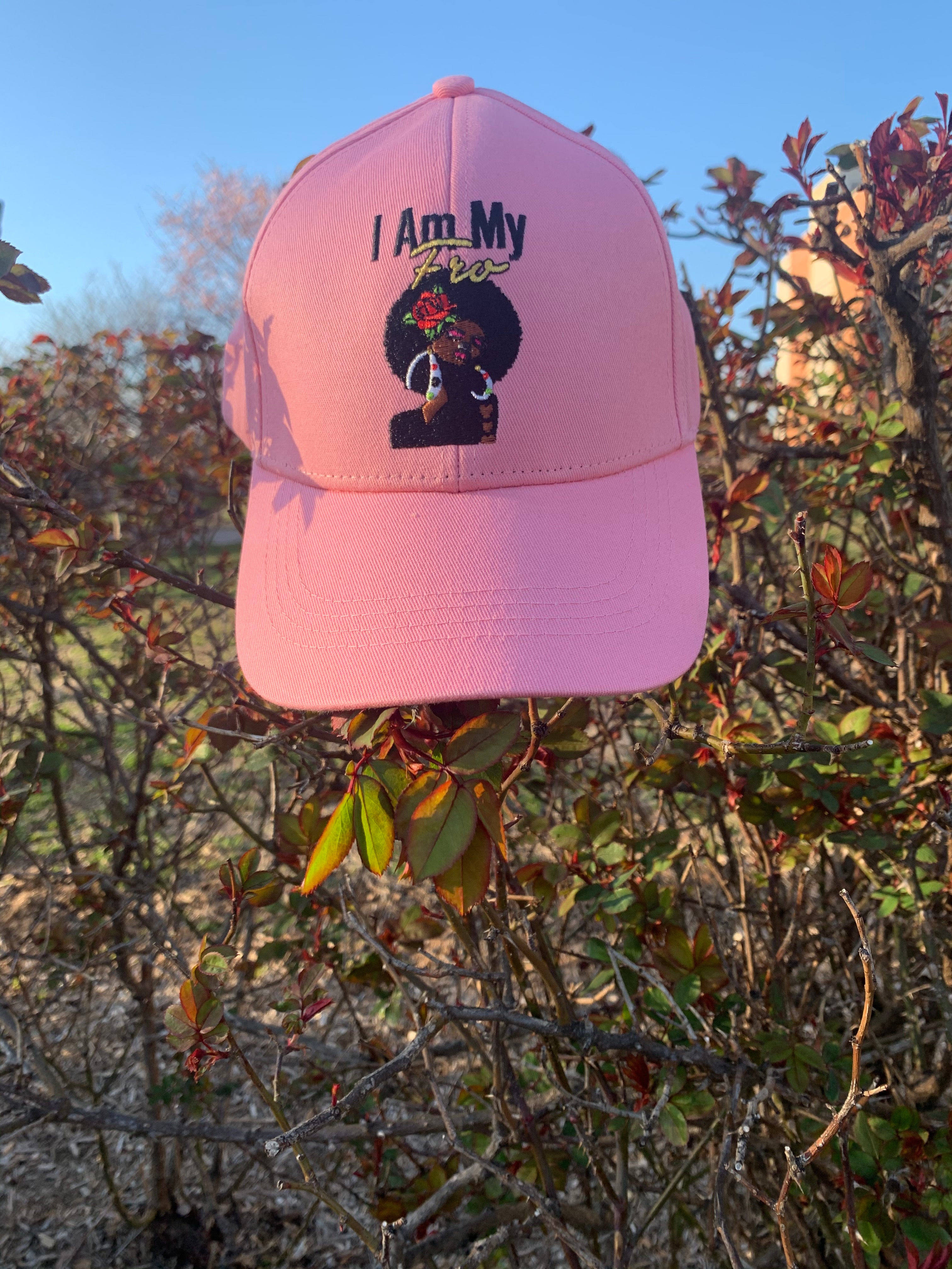 Pink satin-lined basball cap displayed on outdoor foliage.