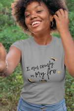 Woman smiling in the woods wearing a grey t-shirt with a custom design and jeans..