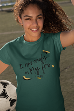 Woman smiling and taking a selfie with a soccer ball in a parking lot wearing a green t-shirt with a custom design.